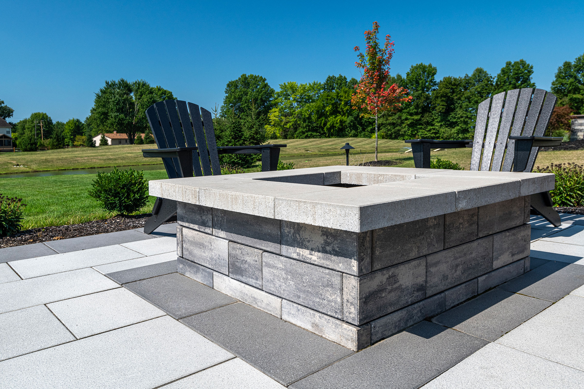Square stone fire pit with black adirondack chairs